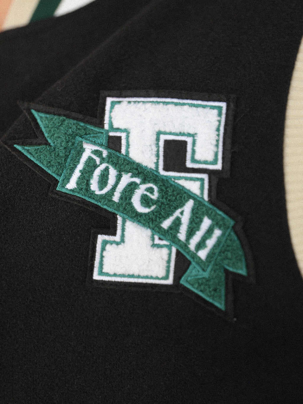 Close-up of the 'Captain's Jacket' from the Royal Collection, showcasing its autumn-inspired hues. Features include exclusive capsule patches, color blocking, black/green checkered lining, and 'Fore All' embroidery on the back. This vintage-inspired varsity jacket combines classic style with modern details, ideal for making a statement in your fall wardrobe.